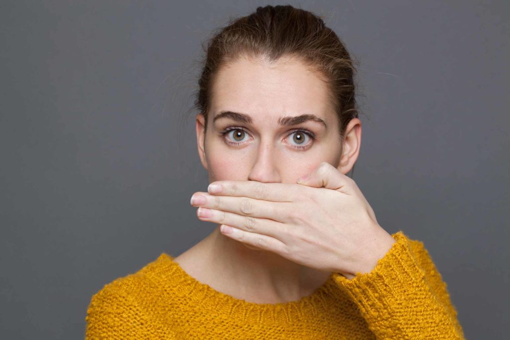 بوی بد دهان خانمی که به دلیل هالیتوز یا بوی بد دهان، دستش را جلوی دهانش قرار داده